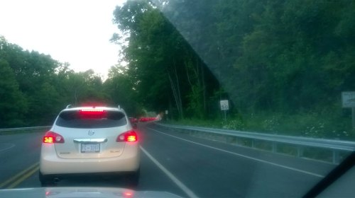 Traffic on a winding road surrounded by trees, with a speed limit sign visible.