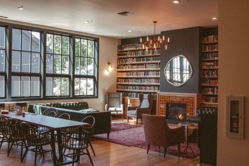 Cozy library with large windows, bookshelves, a fireplace, and comfortable seating areas. Warm, inviting atmosphere.