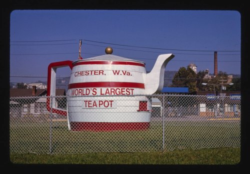 A large teapot sculpture with "World's Largest Teapot" and "Chester, W.Va." painted on it, surrounded by a fence.