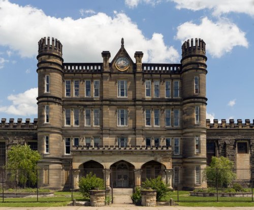 Historic stone building with castle-like towers and a clock, set against a blue sky with fluffy clouds.