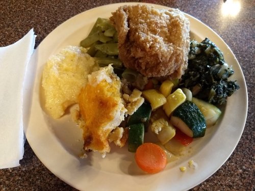 A plate of food featuring fried chicken, greens, mixed vegetables, grits, and a cheesy casserole.
