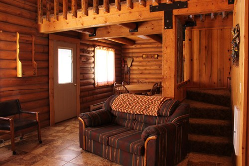 Cozy log cabin interior featuring a sofa, dining area, and wooden staircase. Warm, rustic decor with natural light.
