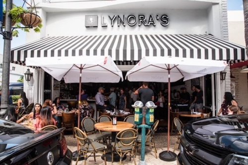 Exterior of Lynora's restaurant with striped awning, outdoor seating, and patrons enjoying their meals.