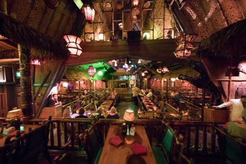 A vibrant, tropical-themed restaurant interior with tiki decor, dim lighting, and wooden seating.
