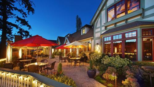A cozy outdoor dining area with umbrellas, surrounded by greenery, at dusk with warm lighting on a charming building.