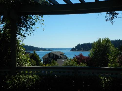 A scenic view of a calm bay framed by greenery and houses, with hills in the background under a clear blue sky.