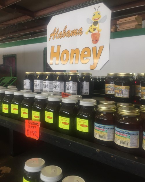 Display of jars of Alabama honey on a shelf, with a sign featuring a bee and prices listed.