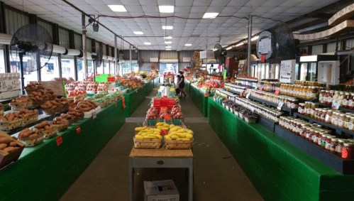 A vibrant market interior filled with colorful fruits, vegetables, and jars of preserves on display.