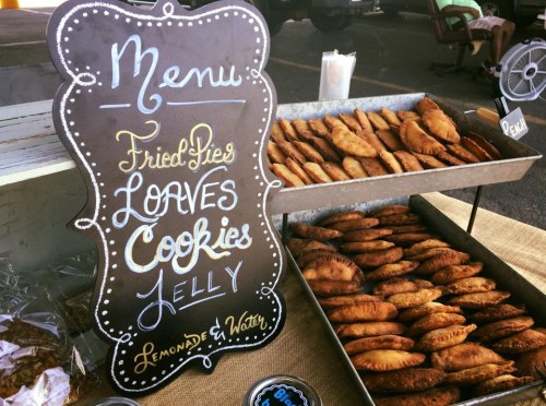 A chalkboard menu displays fried pies, loaves, cookies, jelly, lemonade, and water, with baked goods in metal trays.