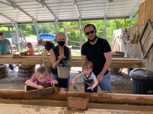 A woman and a man assist two young children in a hands-on activity at an outdoor workshop, all wearing masks.