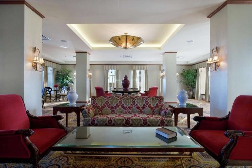 Elegant hotel lobby featuring red chairs, a patterned sofa, a glass coffee table, and decorative lighting.