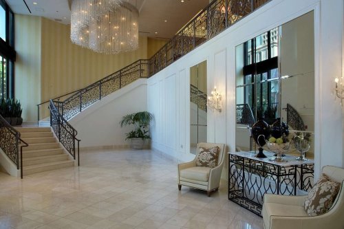 Elegant lobby with a grand staircase, chandeliers, mirrors, and stylish seating. Bright and inviting atmosphere.