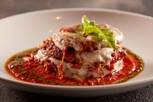 A plate of lasagna topped with melted cheese and fresh basil, served in a rich tomato sauce.