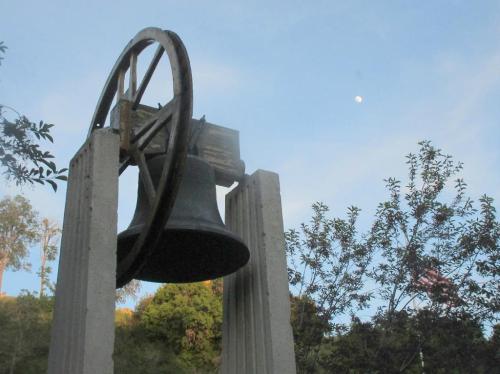 A large bell hangs from a wooden structure, with a clear sky and a crescent moon in the background.