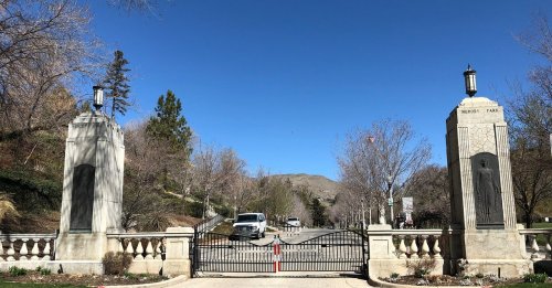 Gates of a park with stone pillars, flanked by trees and a clear blue sky in the background.