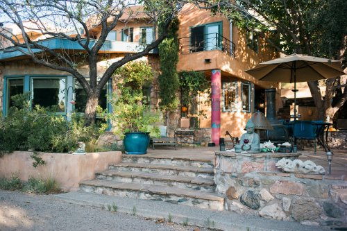 A charming outdoor space with stone steps, potted plants, and a patio umbrella near a colorful house surrounded by trees.