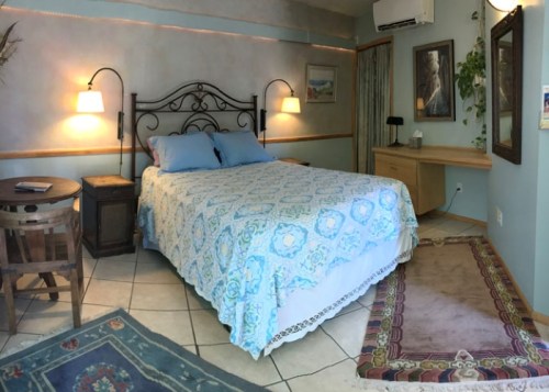 Cozy bedroom featuring a bed with a blue patterned quilt, wooden furniture, and soft lighting.