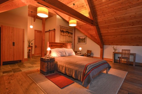 Cozy bedroom with wooden beams, a large bed, warm lighting, and rustic decor, creating a serene atmosphere.