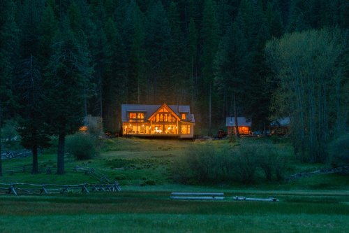 A cozy cabin illuminated at night, surrounded by tall trees and a grassy field.