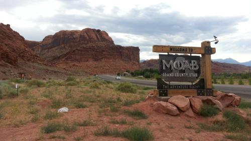 Welcome sign for Moab, Utah, with red rock formations and a cloudy sky in the background.
