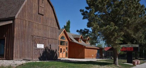 A wooden building with a sign reading "Welcome to Monticello" and a nearby museum, surrounded by trees and blue sky.