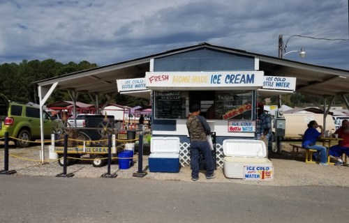 A small ice cream stand with a sign reading "Fresh Home-Made Ice Cream," surrounded by outdoor vendors and customers.