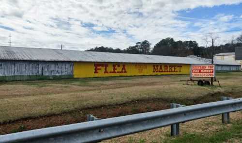 A colorful sign for "Mountain Top Flea Market" on a building, with a grassy area and cloudy sky in the background.