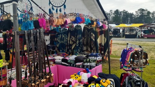 A vibrant market stall displaying colorful clothing, accessories, and plush toys under a tent.