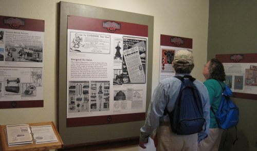Two visitors examine historical display panels in a museum, featuring text and images about local history.