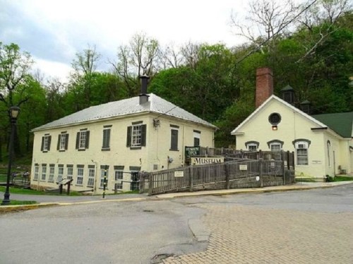 Historic museum building surrounded by trees, featuring a white exterior and a wooden fence at the entrance.