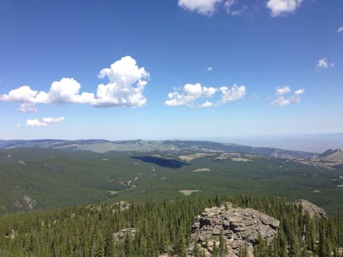 A panoramic view of lush green mountains under a bright blue sky with fluffy white clouds.
