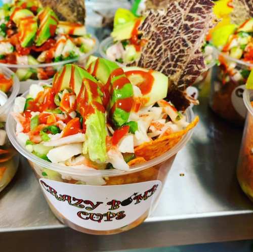Colorful salad in a clear cup, topped with avocado, lettuce, and drizzled with sauce, served with a crispy chip.
