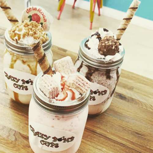 Three colorful milkshake jars topped with whipped cream, cookies, and decorative straws on a wooden table.