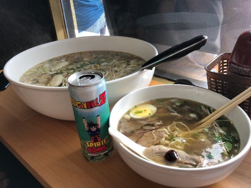 Two bowls of ramen with broth, noodles, and toppings, alongside a can of energy drink featuring a cartoon character.