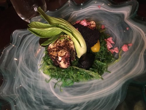 A colorful dish featuring octopus, seaweed, and garnishes, presented in a decorative bowl.