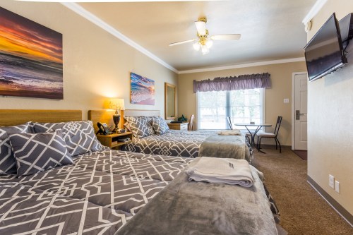 Cozy hotel room with two beds, a table, and a window, featuring warm decor and a beach-themed painting.