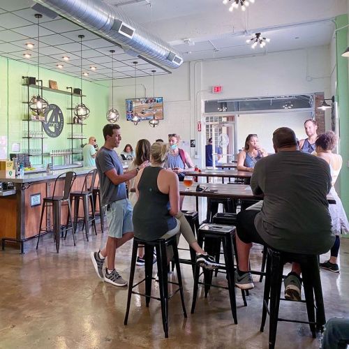 A lively bar scene with patrons chatting and enjoying drinks at high tables in a bright, modern space.