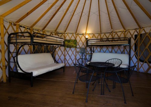 Interior of a yurt featuring bunk beds, futons, and a dining table with chairs, all set in a cozy, rustic style.