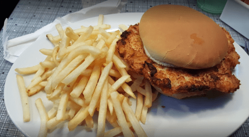 A plate with a crispy chicken sandwich on a bun and a side of golden French fries.