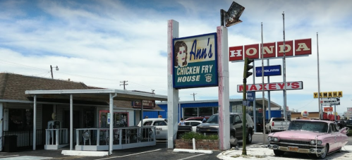 A roadside scene featuring a retro sign for "Ann's Chicken Fry House" and nearby car dealerships.