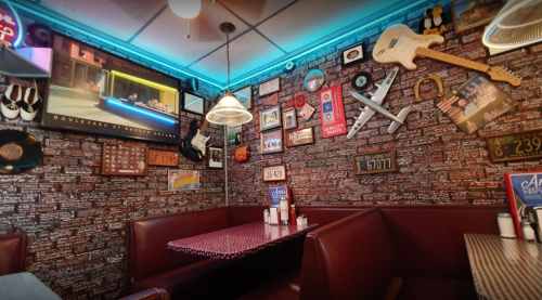 Cozy diner booth with red leather seating, vintage decor, and a neon-lit ceiling, featuring various memorabilia on the walls.