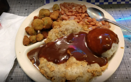 A plate of food featuring fried chicken, gravy, mashed potatoes, baked beans, and fried okra on a checkered tablecloth.