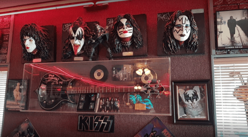 A wall display featuring KISS band masks, a guitar, records, and framed photos in a vibrant, rock-themed setting.