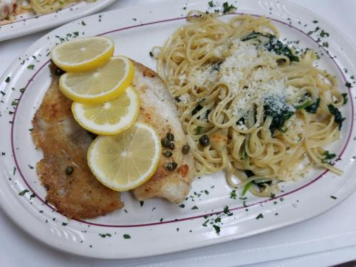 A plate of grilled fish with lemon slices, served alongside linguine pasta with spinach and grated cheese.