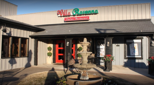 Exterior of Villa Ravenna Italian Restaurant featuring a fountain and red doors, with a sign above the entrance.