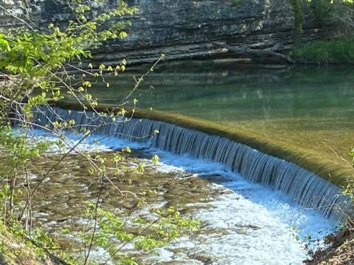 A serene river scene featuring a gentle waterfall cascading over a rocky ledge, surrounded by lush greenery.
