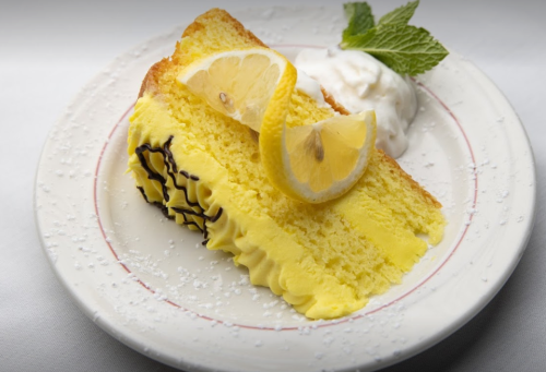A slice of lemon cake topped with lemon slices and a dollop of whipped cream, garnished with mint leaves.