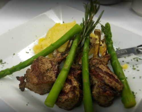 Grilled lamb chops served with asparagus and creamy mashed potatoes, garnished with herbs on a white plate.