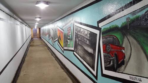 A long tunnel with a painted mural featuring vintage cars and Route 66 imagery on the walls.