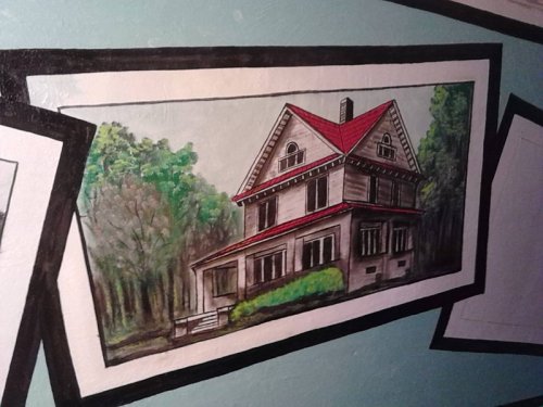 A painted illustration of a large house with a red roof, surrounded by trees, framed on a wall.